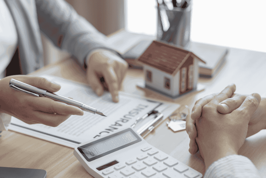 Conseiller montrant un contrat de prêt avec une maison miniature en arrière-plan.