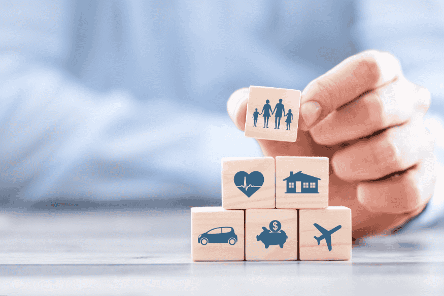 Main plaçant un cube avec une famille au sommet d’autres cubes représentant des besoins assurés.