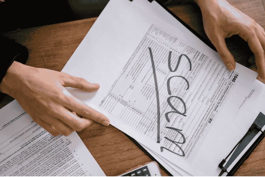 Main tenant un document avec la mention "scam" écrite en travers d’un formulaire.