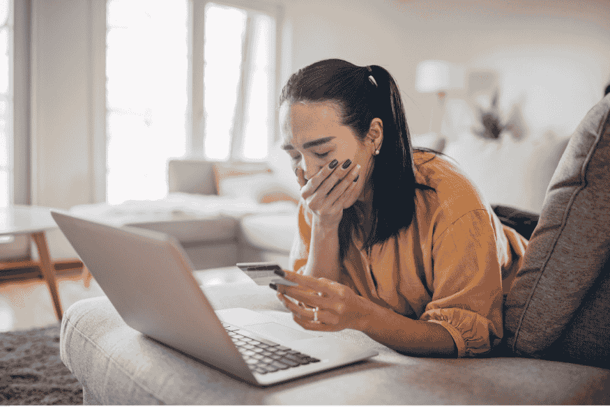 Femme préoccupée tenant une carte bancaire devant un ordinateur, suspectant une fraude.