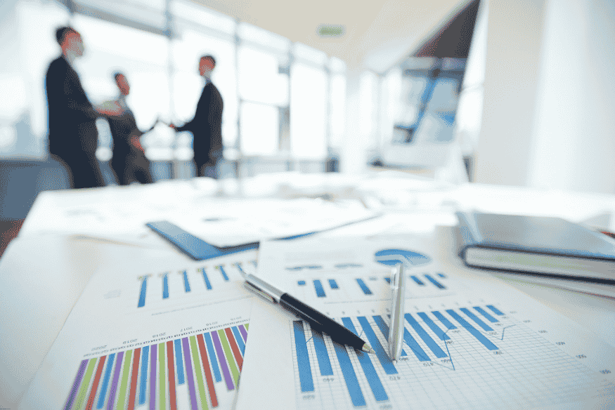 Documents financiers avec graphiques en barres sur une table, en arrière-plan des professionnels se serrent la main