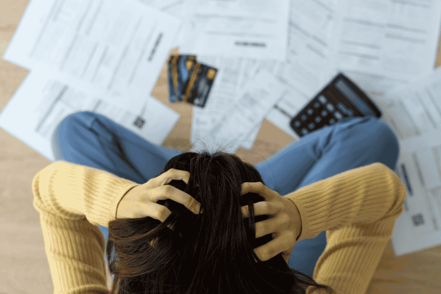 Femme assise par terre entourée de factures, cartes de crédit et une calculatrice, les mains sur la tête