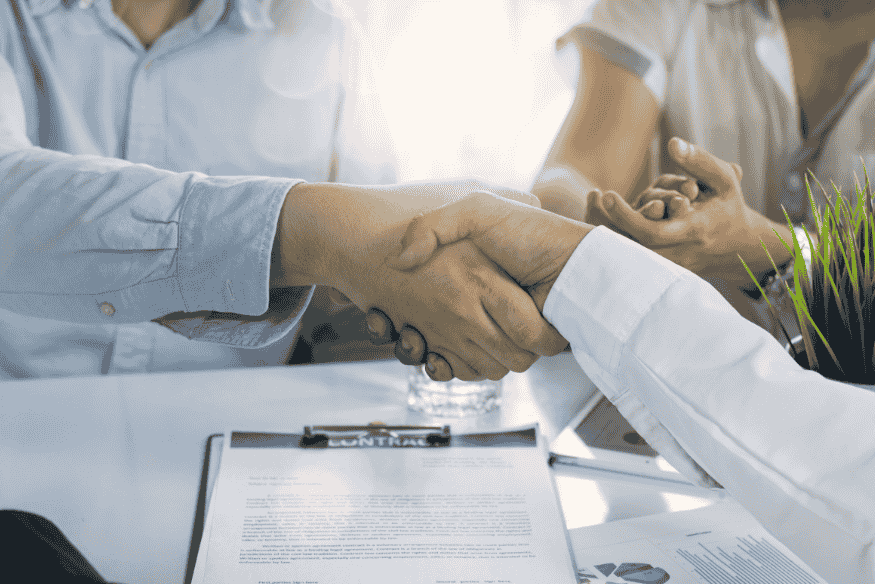 Deux personnes se serrant la main au-dessus d’un contrat signé.