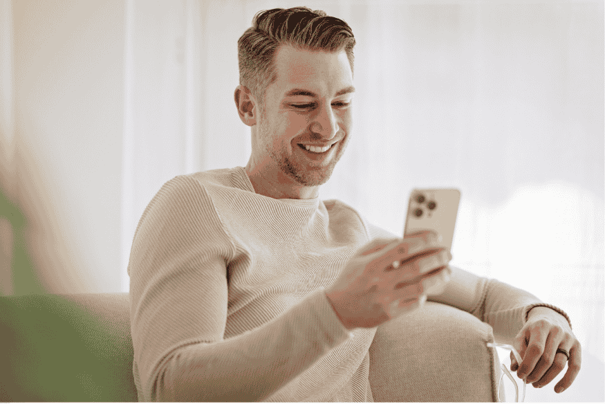 Homme souriant assis sur un canapé regardant son téléphone.