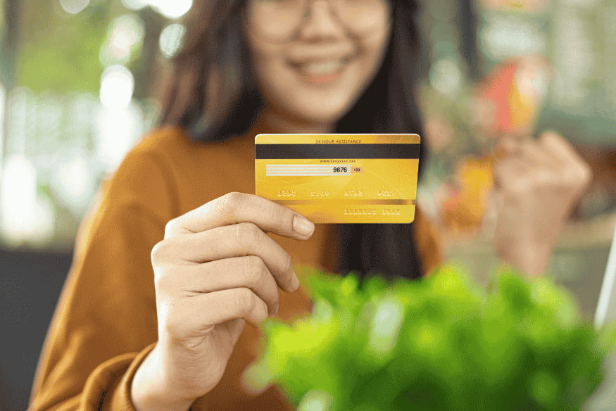 Commerçante souriante présentant une carte bancaire après une transaction réussie via terminal de paiement électronique.