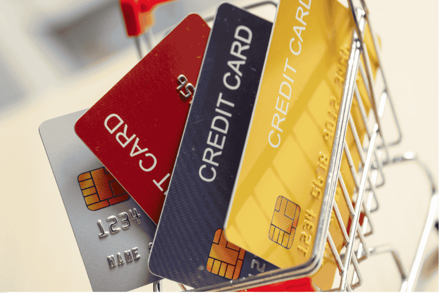 Quatre cartes de crédit de différentes couleurs dans un petit chariot d’achat miniature.