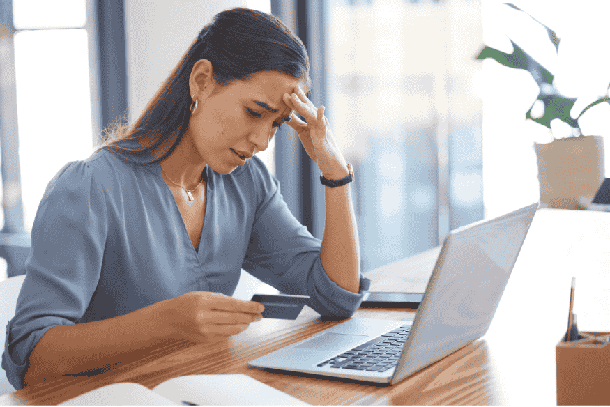 Femme inquiète regardant sa carte bancaire devant un ordinateur portable.