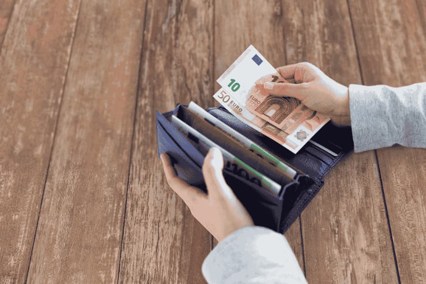 Personne plaçant des billets en euros dans un portefeuille sur une table en bois.