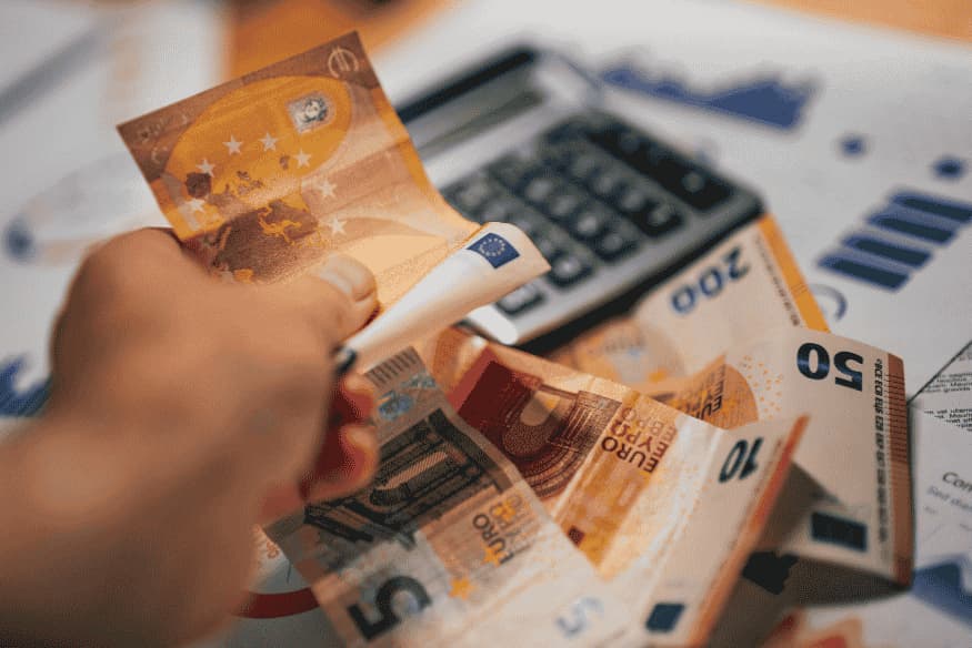 Main tenant plusieurs billets en euros sur fond de graphique financier.