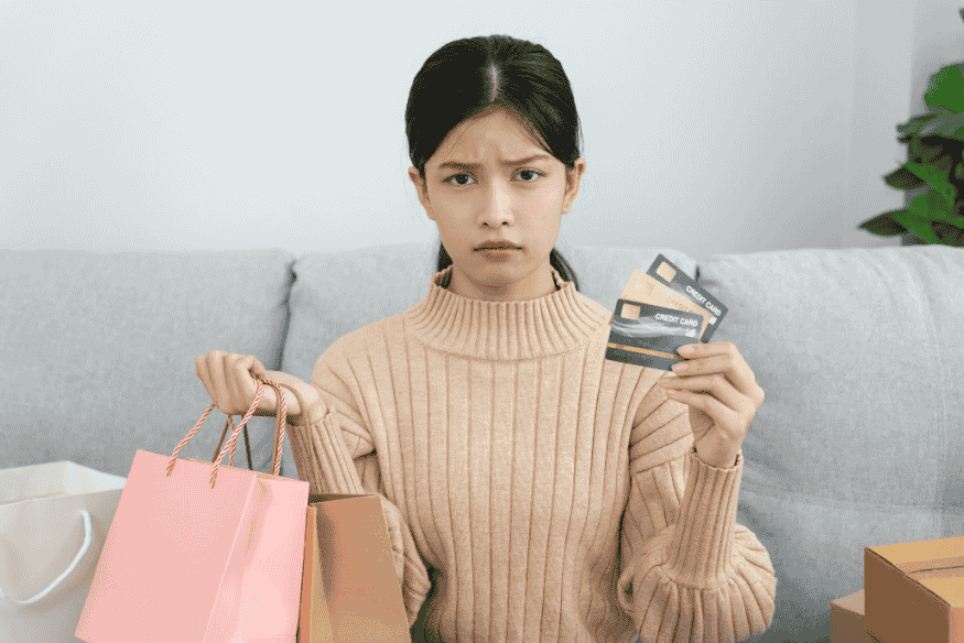 Ragazza con borse della spesa e carte bancarie in mano, immagine che illustra un pagamento rifiutato con carta bancaria durante un acquisto.