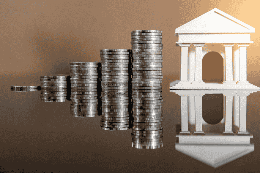 Piles de pièces de monnaie formant une courbe ascendante menant à une maquette de bâtiment bancaire.