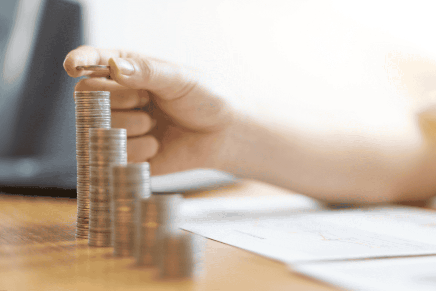 Main empilant des pièces sur un bureau avec des graphiques financiers